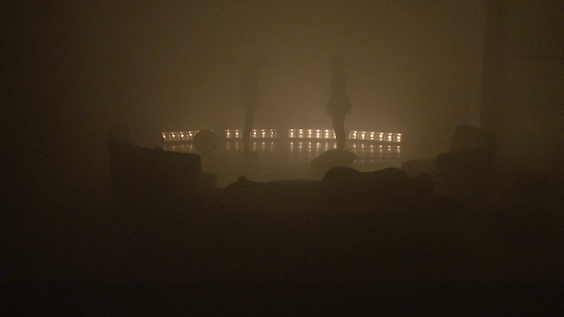 Ein Suchscheinwerfer und Silhouetten verschwinden im dichten Nebel.