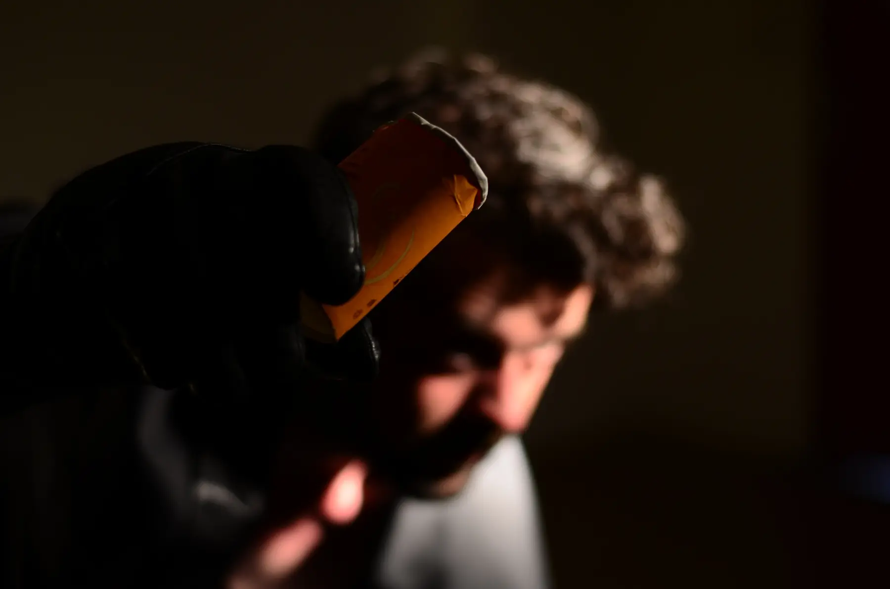 Ein zerknitterter Becher in einer behandschuhten Hand, die Figur unscharf dahinter.