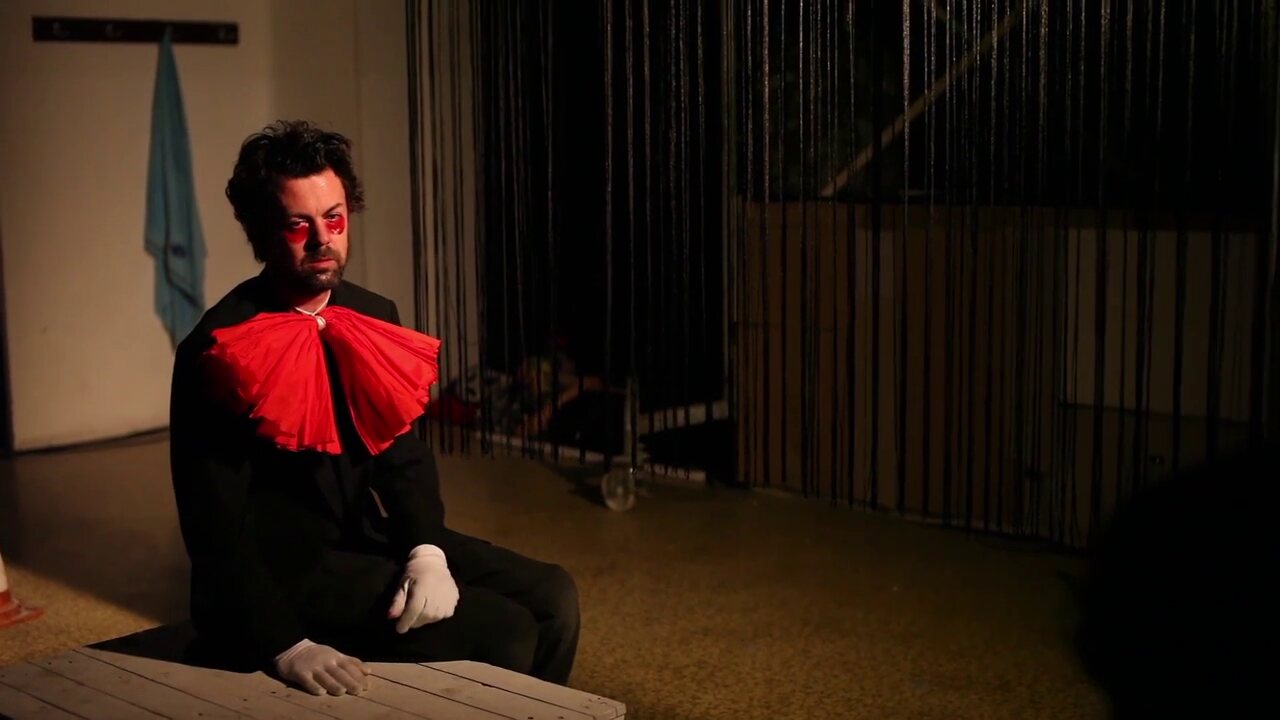Der Clown sitzt allein vor dem dunklen Bühnenvorhang.