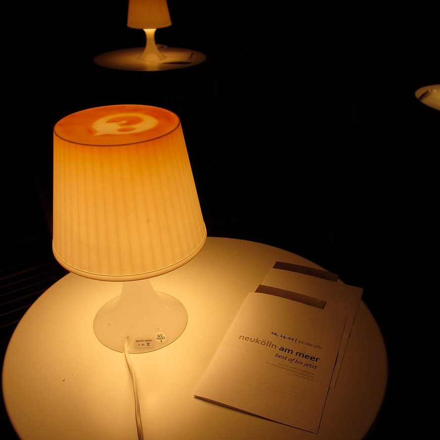Eine kleine leuchtende Tischlampe neben einem Programmheft von Neukölln am Meer.